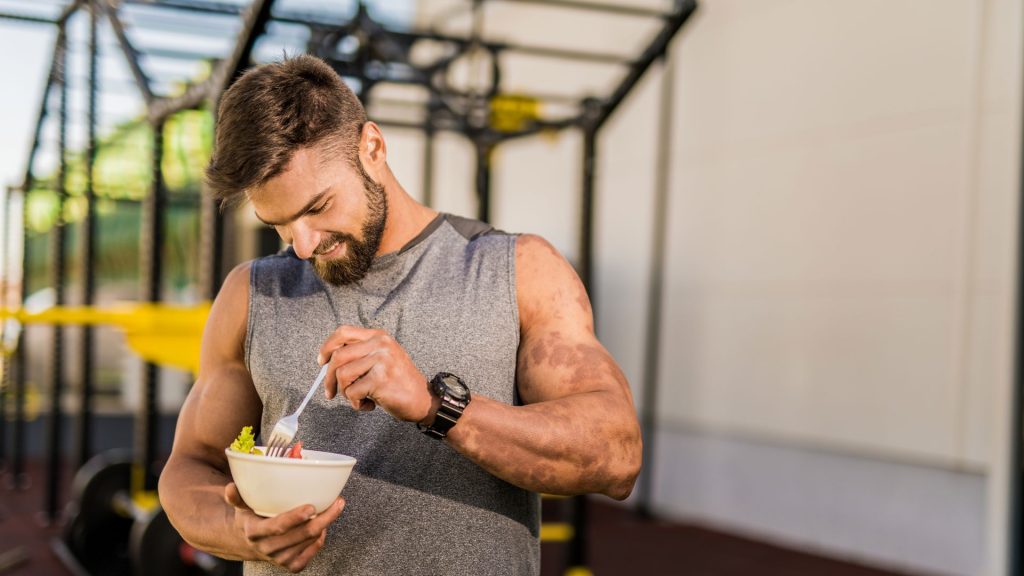Hombre comiendo una comida saludable en el gimnasio, equilibrando su nutrición para ganar masa muscular y reducir grasa corporal
