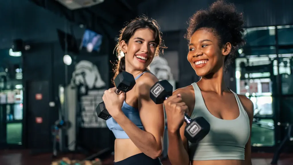 Dos mujeres levantando mancuernas en el gimnasio, entrenando para ganar masa muscular y reducir grasa corporal al mismo tiempo
